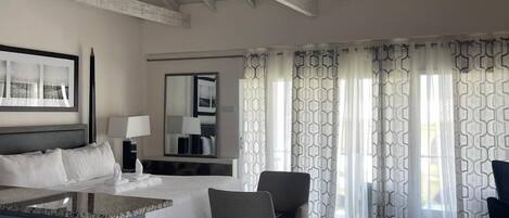 Habitación de hotel con cama, escritorio, sillas, ventilador de techo y cortinas estampadas.