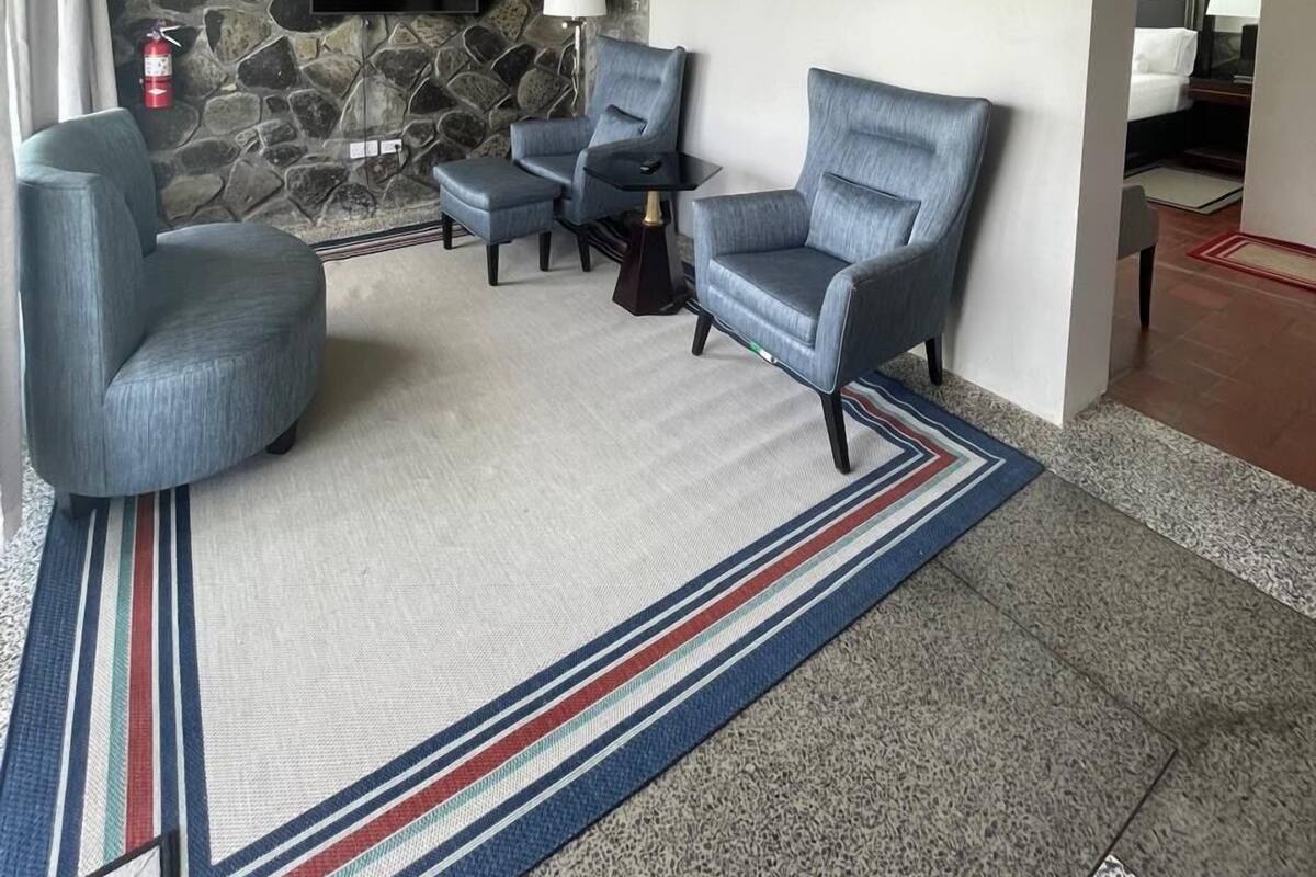 A modern living room with a stone wall, a mounted TV, two armchairs, a side table, and a patterned rug.