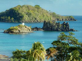A tropical island with a white cross on a small rock, surrounded by clear blue waters and lush greenery.
