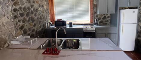 A kitchen with a stone wall, wooden ceiling, and a window with blinds.