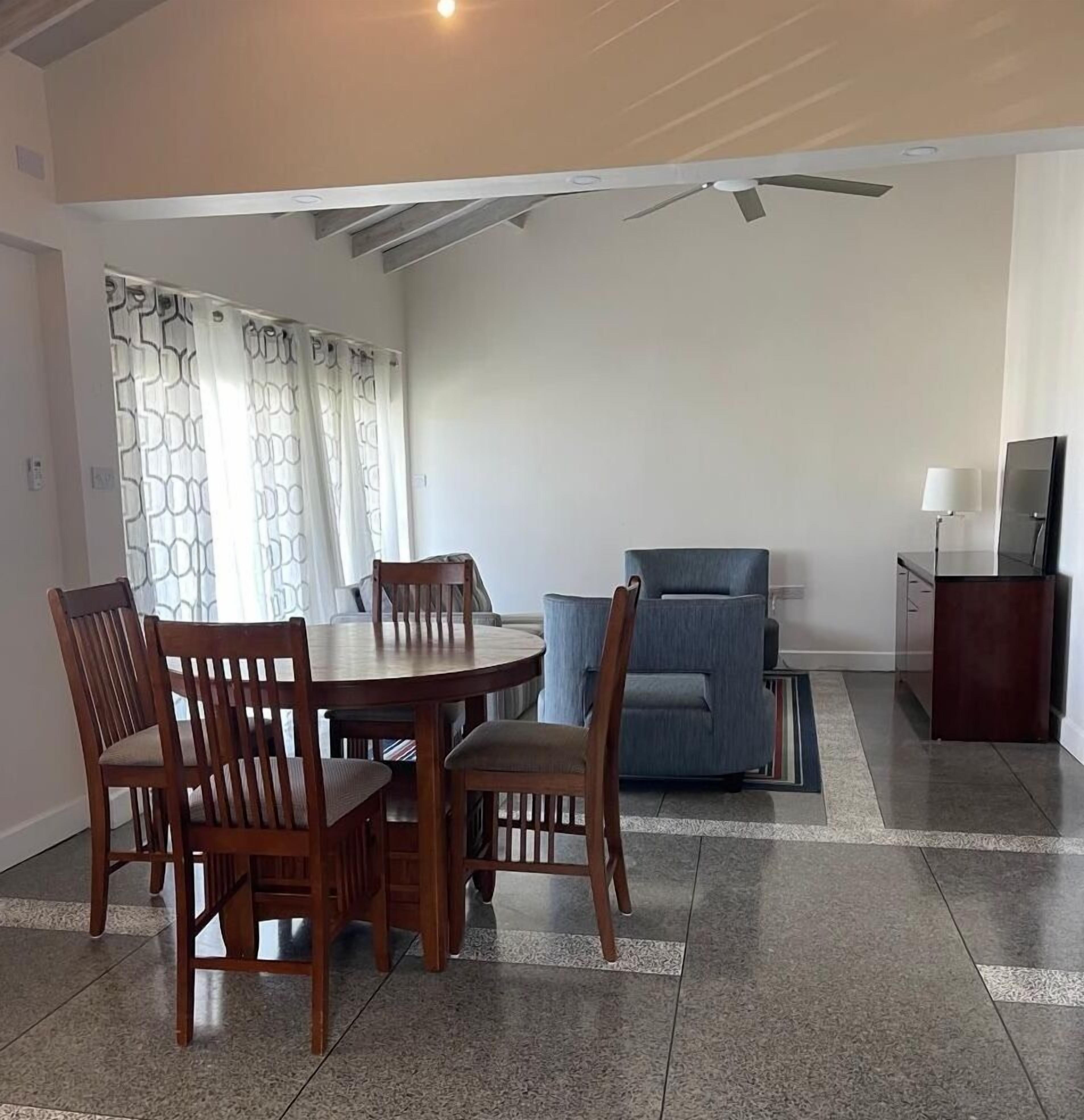A dining area with a round table and chairs, a blue sofa, a TV, and a lamp.