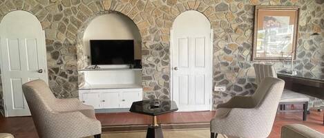 Une pièce chaleureuse avec une cheminée en pierre, deux fauteuils, un canapé, un ventilateur de plafond et un téléviseur.