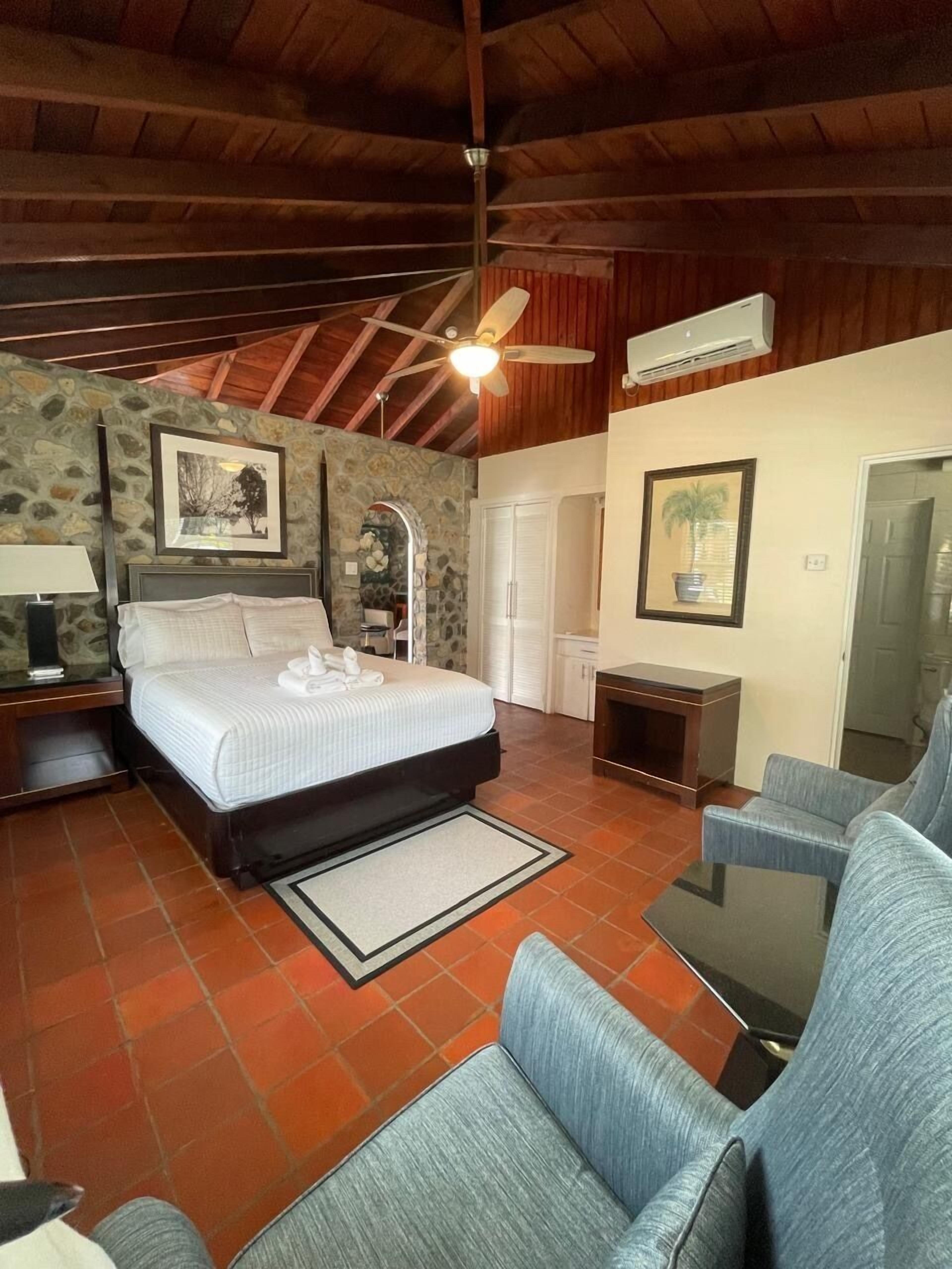 Une chambre à coucher comprenant un lit, une table de chevet, une chaise, une petite table et un ventilateur de plafond.
