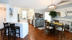 A modern kitchen with a central island, wooden bar stools, and a dining area with a table and chairs. - 3 BR Beach House in Surfside Beach! Raycliff at the Beach (Surfside Beach)