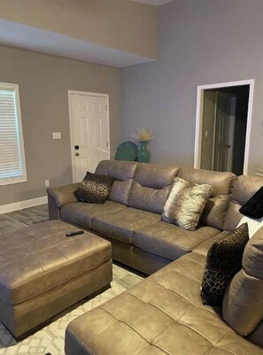 Relax in this inviting living room with a comfortable sofa and ottoman, a door, and a window with blinds.