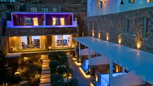 A modern two-story building with a glass facade, outdoor seating area, and a stone wall. - VILLA PANAMERA,  Infinite view, Private heaven (Mykonos)