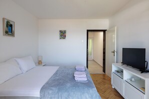 Une chambre à coucher comprenant un lit, un téléviseur, une table de chevet et une porte donnant sur une autre pièce.