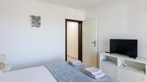 Ein Schlafzimmer mit einem Bett, einem Fernseher auf einem Schrank, einer Tür und einem kleinen Regal mit Gegenständen.