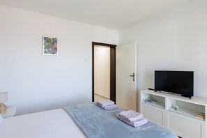 A bedroom with a bed, a television on a stand, a door, and a small shelf with items. - Beslema sea view apartment with balcony (Dubrovnik)
