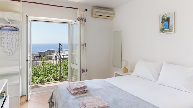 Ein Schlafzimmer mit Bett, Nachttisch, Fenster und Meerblick sowie einer Klimaanlage.