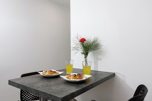 Una mesa de comedor con dos platos de comida, dos vasos de líquido amarillo y un florero con una flor roja.