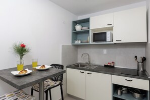 A compact kitchen with a sink, microwave, and cabinets. There is a dining table with chairs and a vase with a flower. - Beslema sea view apartment with balcony (Dubrovnik)