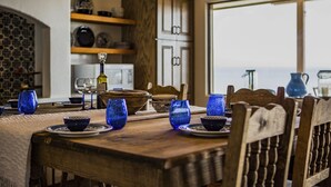 A dining table set with blue glassware, wooden chairs, and a view of the sea through a large window. - Terracotta Villa 117 Bayfront Fireworks Boat Slip View Space X Hot tub (South Padre Island)
