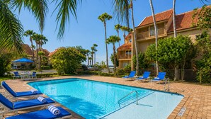 Ein Swimmingpool mit blauen Liegestühlen, Palmen und einem Gebäude mit rotem Ziegeldach.