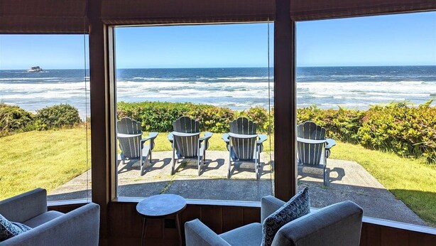 Une pièce dotée de grandes fenêtres donnant sur un espace verdoyant où se trouvent plusieurs fauteuils Adirondack.