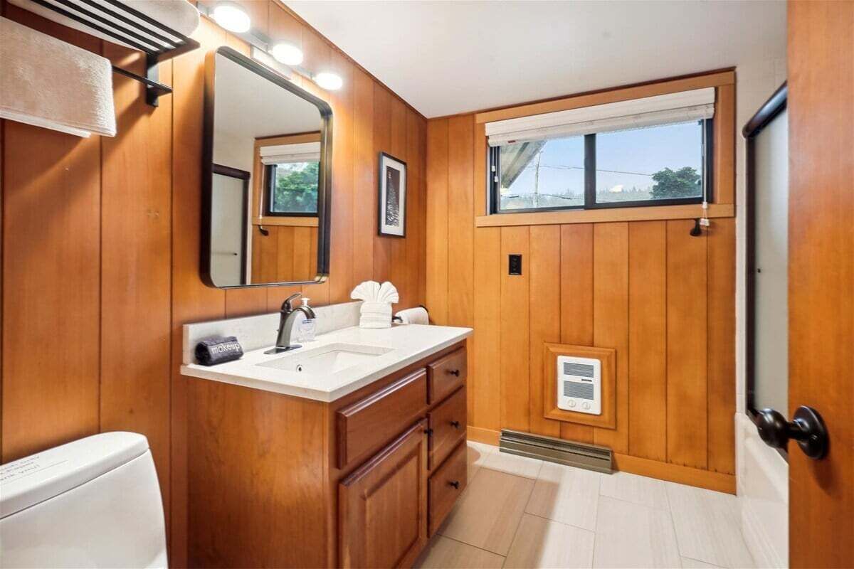 Une salle de bain avec un lambris en bois, un lavabo blanc, un miroir et une fenêtre.