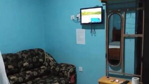 A room with a blue wall, a floral-patterned sofa, a wooden TV stand with a TV, and an air conditioning unit.