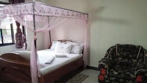 A bedroom with a four-poster bed, a floral armchair, and a window with a view.