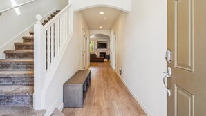Un pasillo con una escalera de madera, un banco y una puerta con cerradura electrónica.