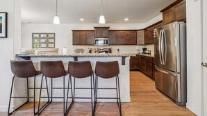 Una cocina moderna con una isla central, taburetes de bar, electrodomésticos de acero inoxidable y armarios de madera.