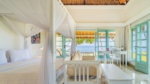 A bedroom with a bed, a bench, a desk, and a view of the sea.