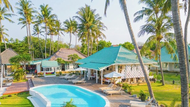 A resort with a swimming pool, lounge chairs, and palm trees.
