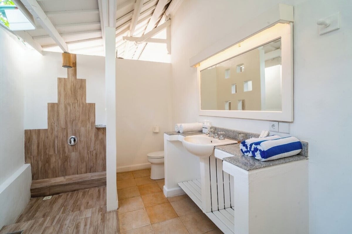 Casa de banho moderna com chuveiro de madeira, lavatório branco e um espelho grande.