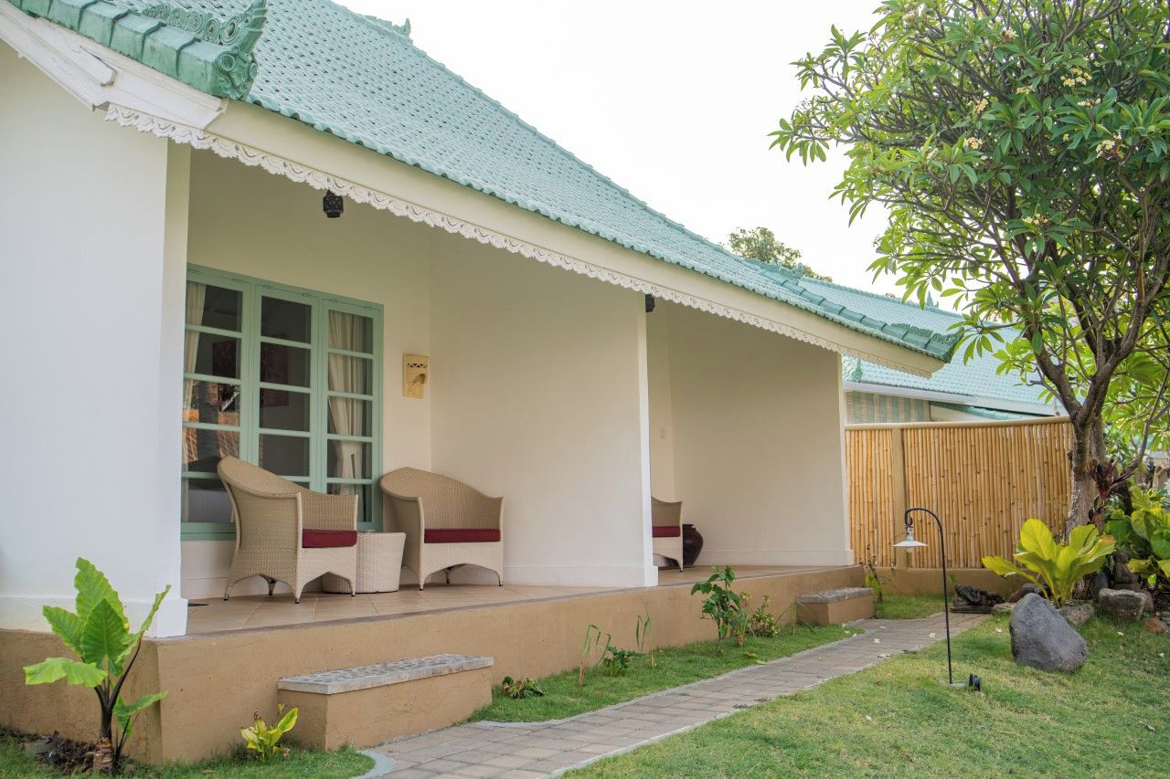 A building with a porch, wicker furniture, a bamboo fence, and a pathway.