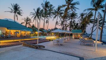 A beachside resort with lounge chairs, umbrellas, and a pool area.
