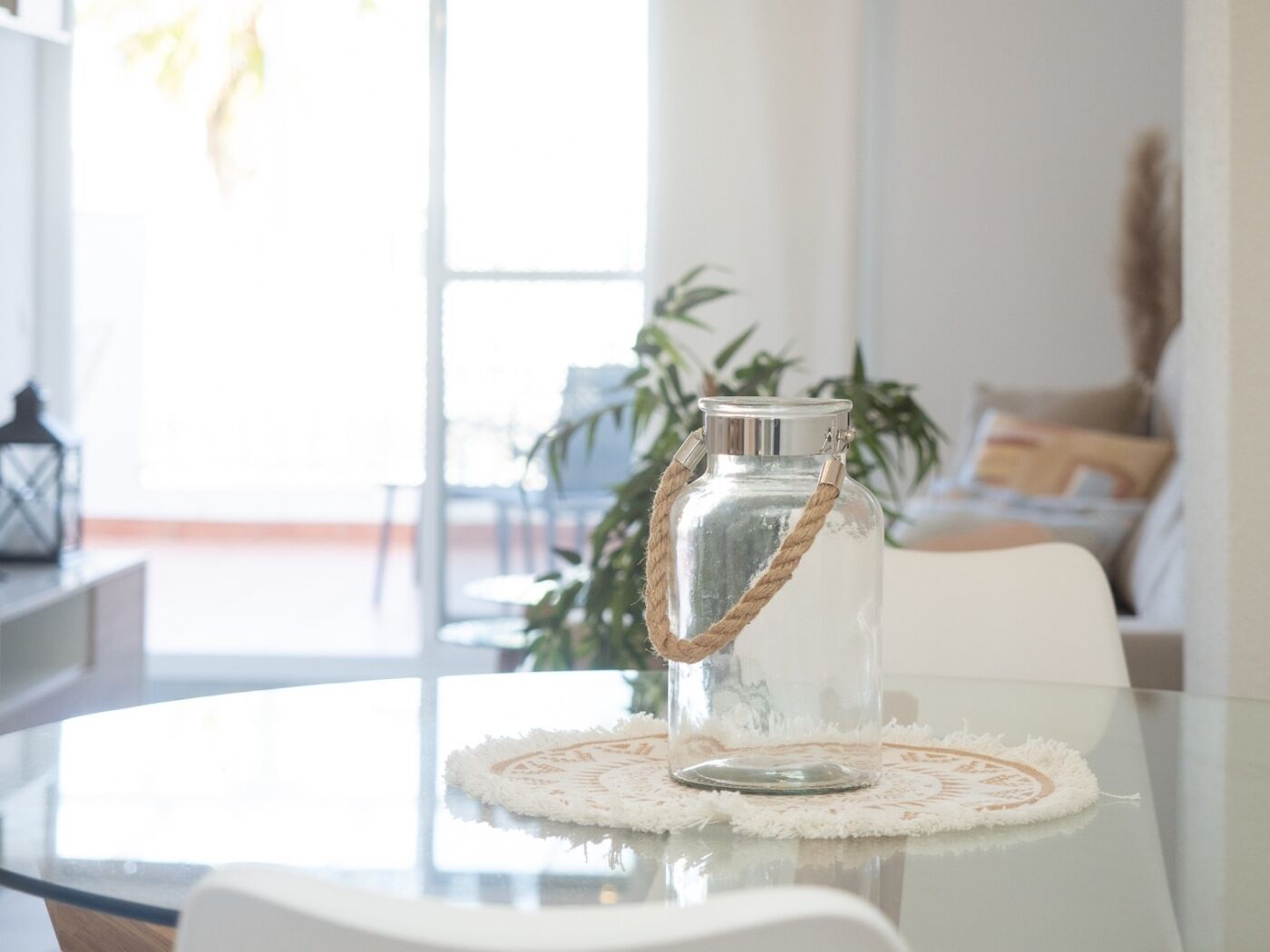 A clear glass pitcher with a rope handle on a glass table with a white coaster.