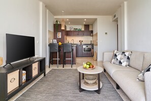 A modern living room with a flat-screen TV, a sofa, a coffee table with fruit, and a kitchen in the background. - Apartment 'Casa Limón' with Sea View, Wi-Fi and Air Conditioning (Nerja)