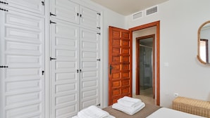 Une chambre d’hôtel avec un lit, une porte en bois, un miroir et une armoire blanche.