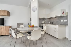 Une cuisine moderne avec des meubles blancs, un plan de travail en granit et un coin repas comprenant une table ronde et des chaises.