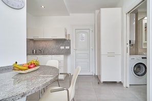 Une cuisine moderne dotée d’un plan de travail en granit, d’un panier de fruits, de meubles blancs et d’un lave-linge encastré.