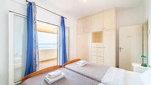 A bedroom with two beds, a wardrobe, a bedside table, and a view through a window. - Apartment 'Alex' with Wi-Fi and Air Conditioning (Corfu)