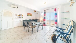 A living room with a sofa, a dining table with chairs, a glass door leading outside, and a small shelf with decorative items. - Apartment 'Alex' with Wi-Fi and Air Conditioning (Corfu)