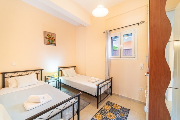 A room with two beds, a small table with a lamp, a window with a view, and a door.