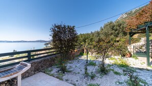 Um pátio com um banco de pedra, vista para o mar e uma pérgula verde.