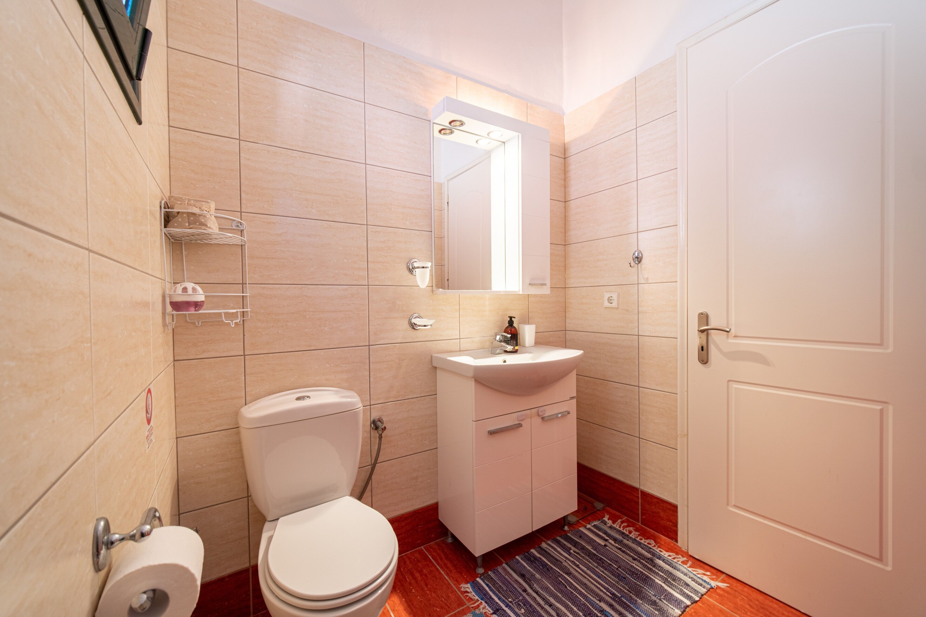 A bathroom with a toilet, sink, mirror, and tiled walls.