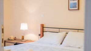Cama bem arrumada com lençóis brancos, abajur e quadro na parede.