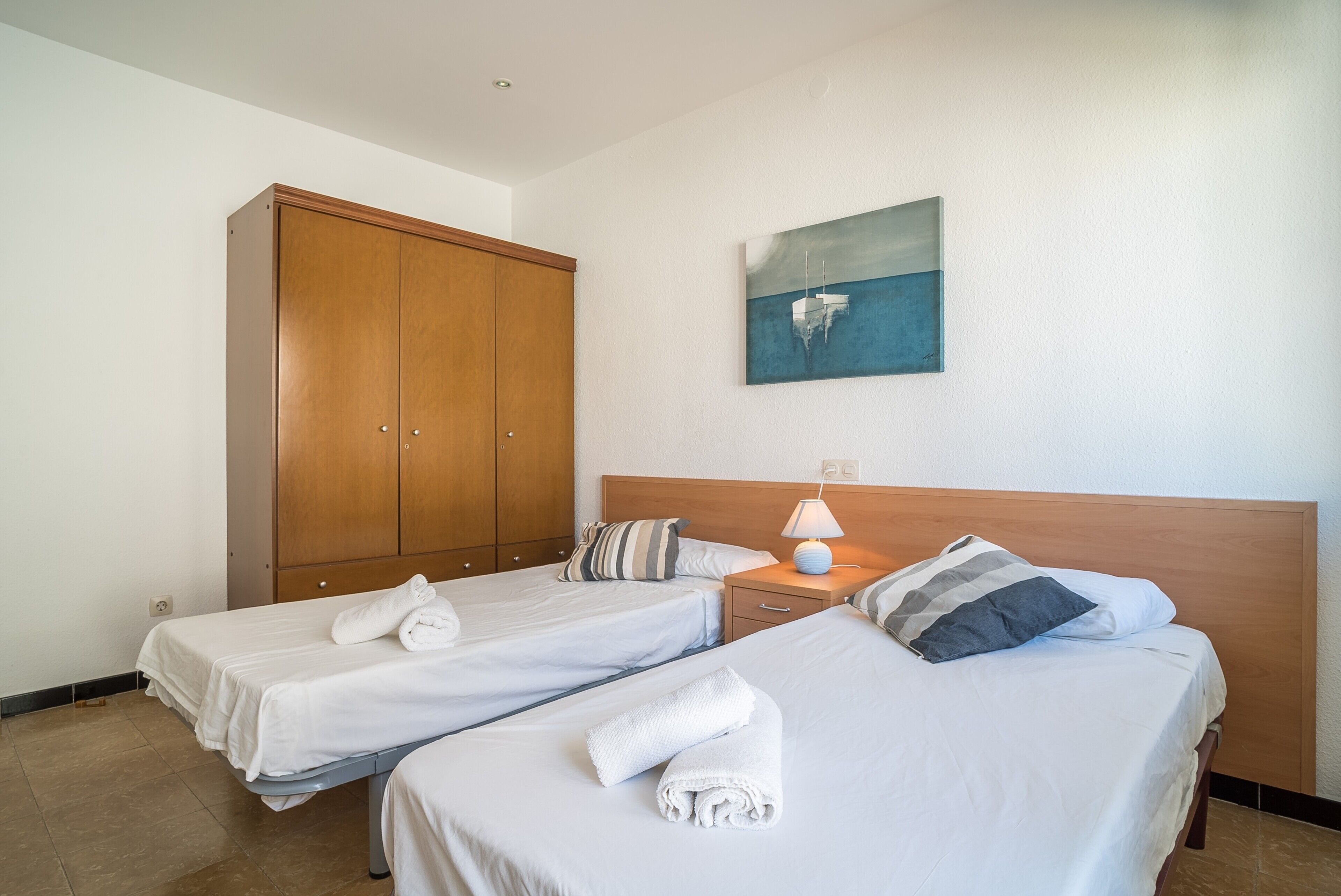 Ein Hotelzimmer mit zwei Einzelbetten, einem Holzschrank, einem Nachttisch mit Lampe und einem Bild an der Wand.
