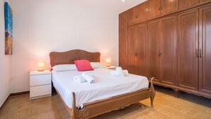 A bedroom with a wooden bed, white bedding, a nightstand with a lamp, and a wardrobe.