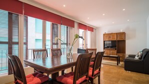 A dining area with a wooden table and chairs, a vase with flowers, and a kitchen area with cabinets and a TV.