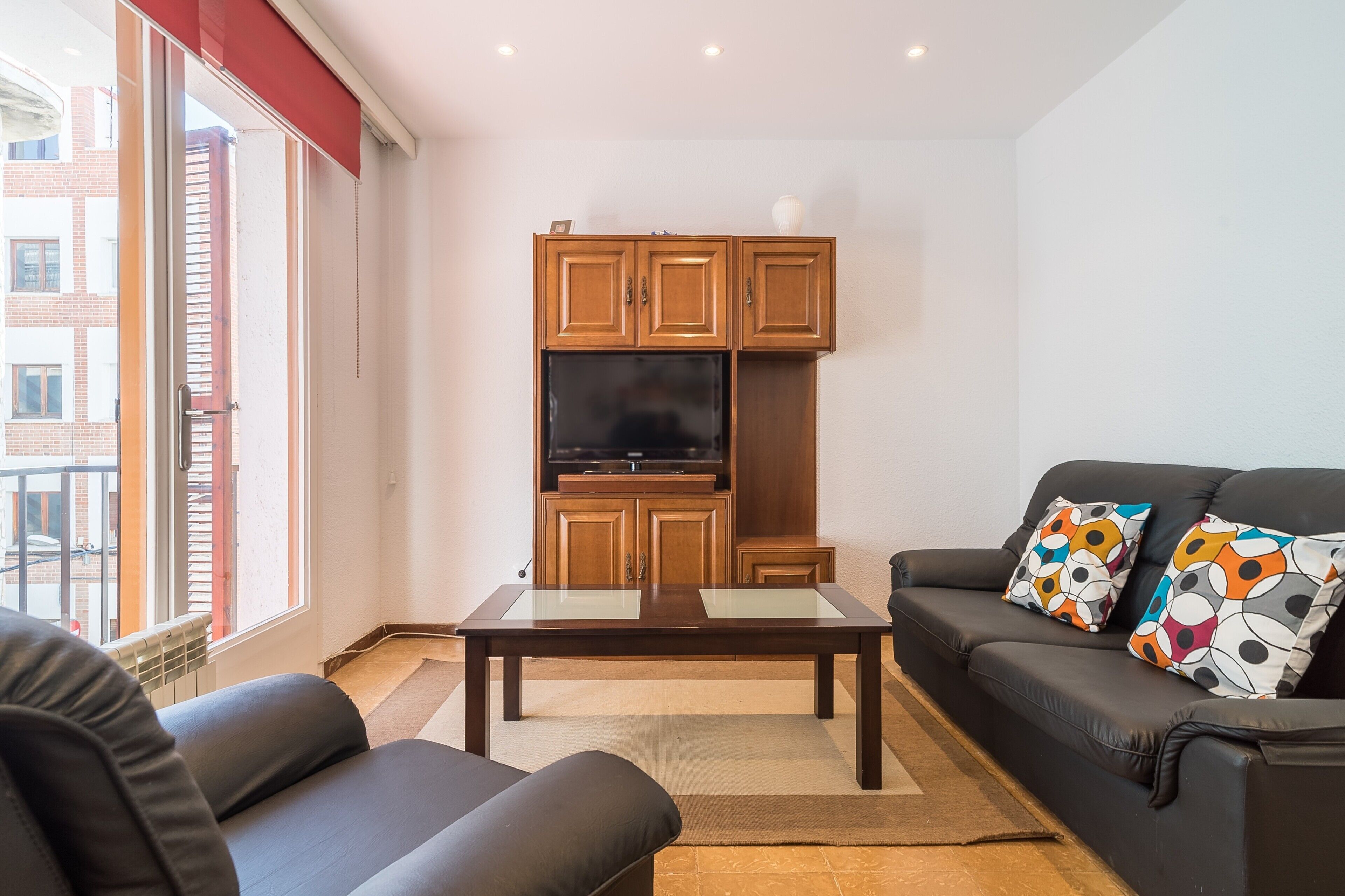 Un salon comprenant un canapé, une table basse avec un plateau en verre et des meubles en bois, dont un meuble pour la télévision.