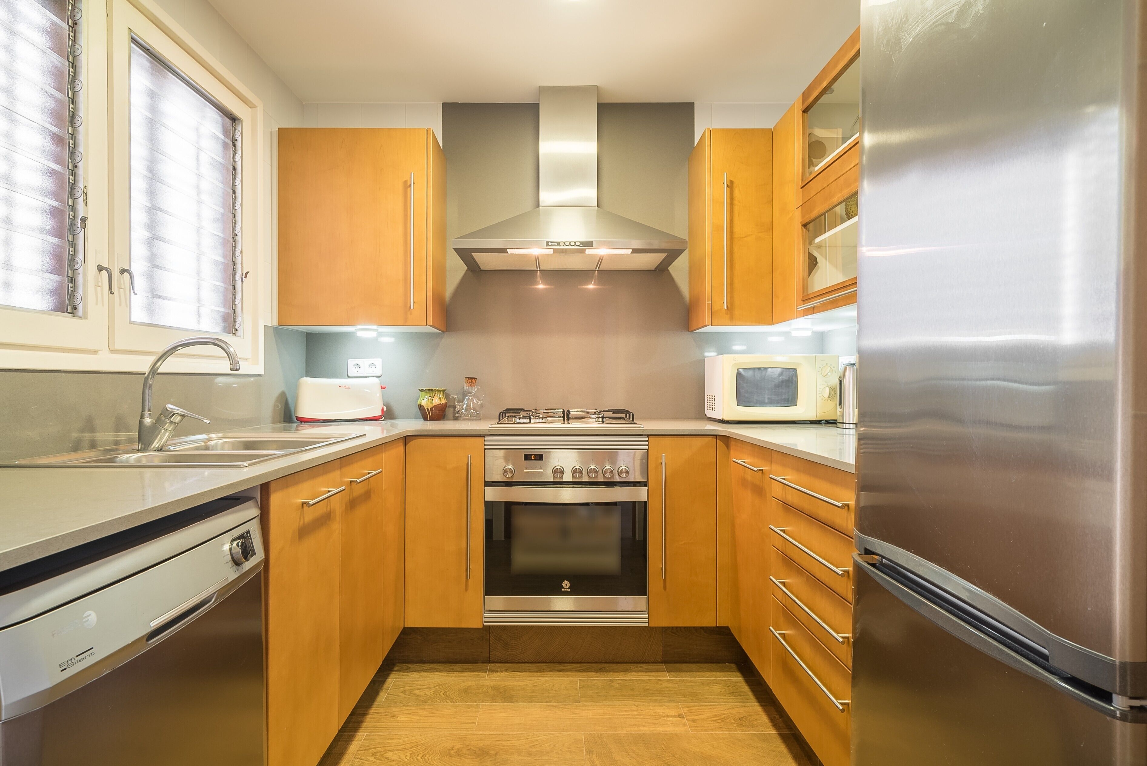 A compact kitchen with wooden cabinets, a stainless steel oven, a microwave, and a refrigerator.