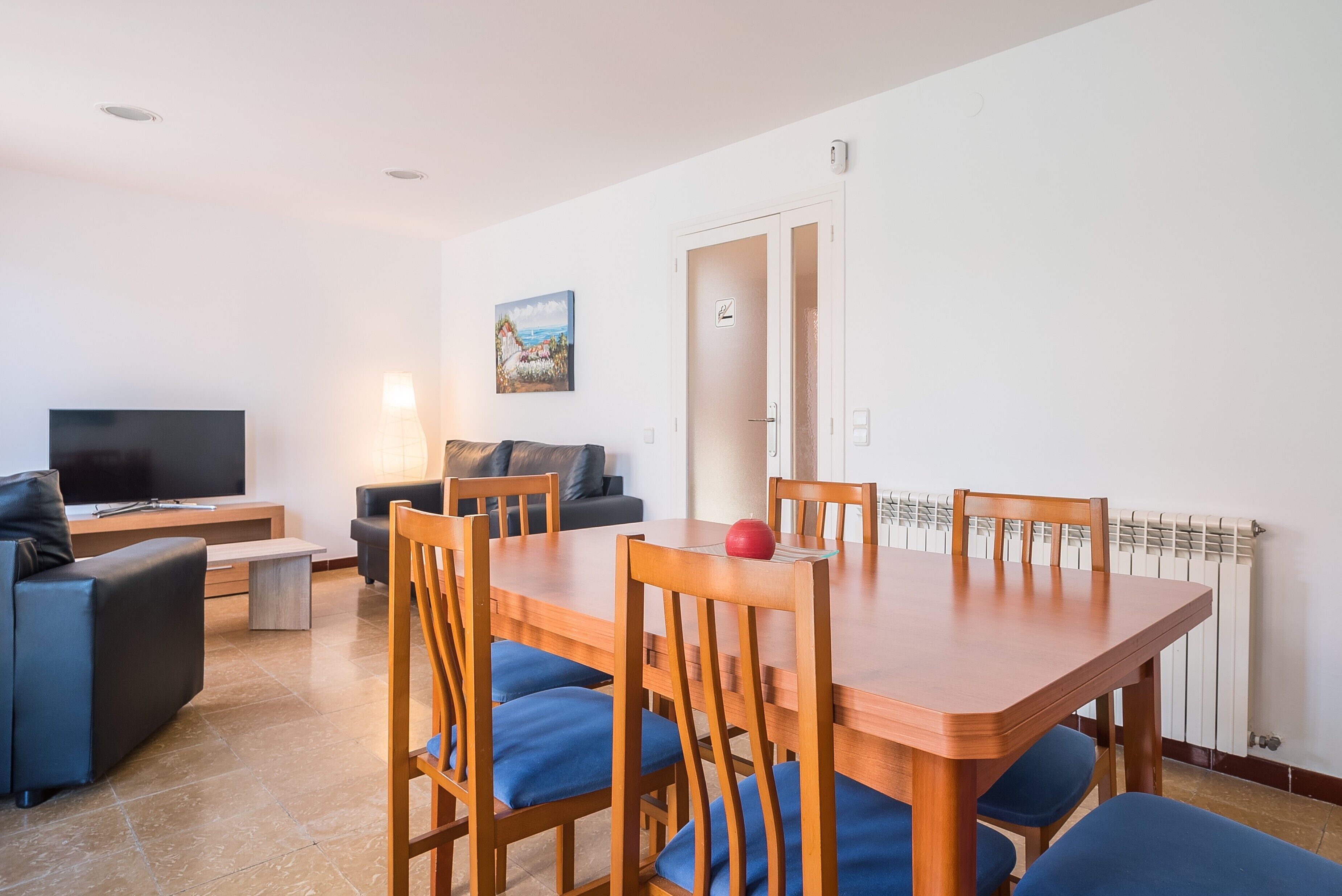 Una sala moderna con televisor, sofá y mesa de comedor con sillas.