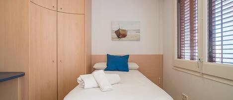 A bedroom with a bed, a wooden wardrobe, a window with blinds, and a painting on the wall.