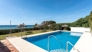 Una piscina con vista al mar, rodeada de un césped cuidado y un edificio blanco.
