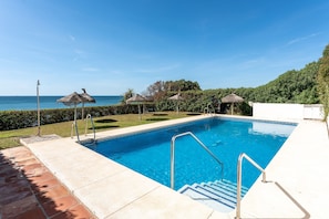 Una piscina con vista al mar, rodeada de un césped cuidado y un edificio blanco.