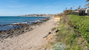 Una playa con costa rocosa, una playa de arena y un edificio con techo plano.